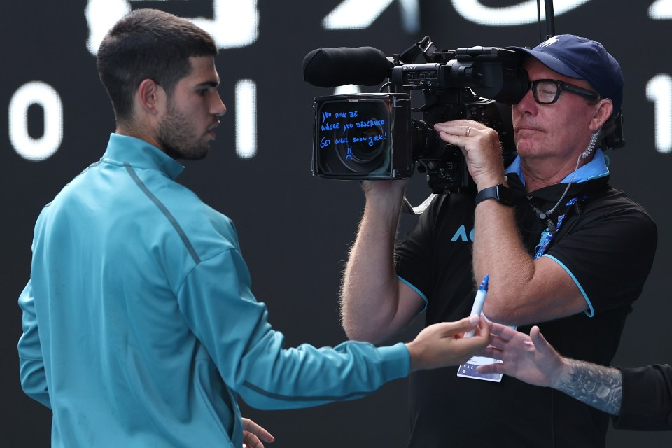 Carlos Alcaraz writing a get-well message on a camera.