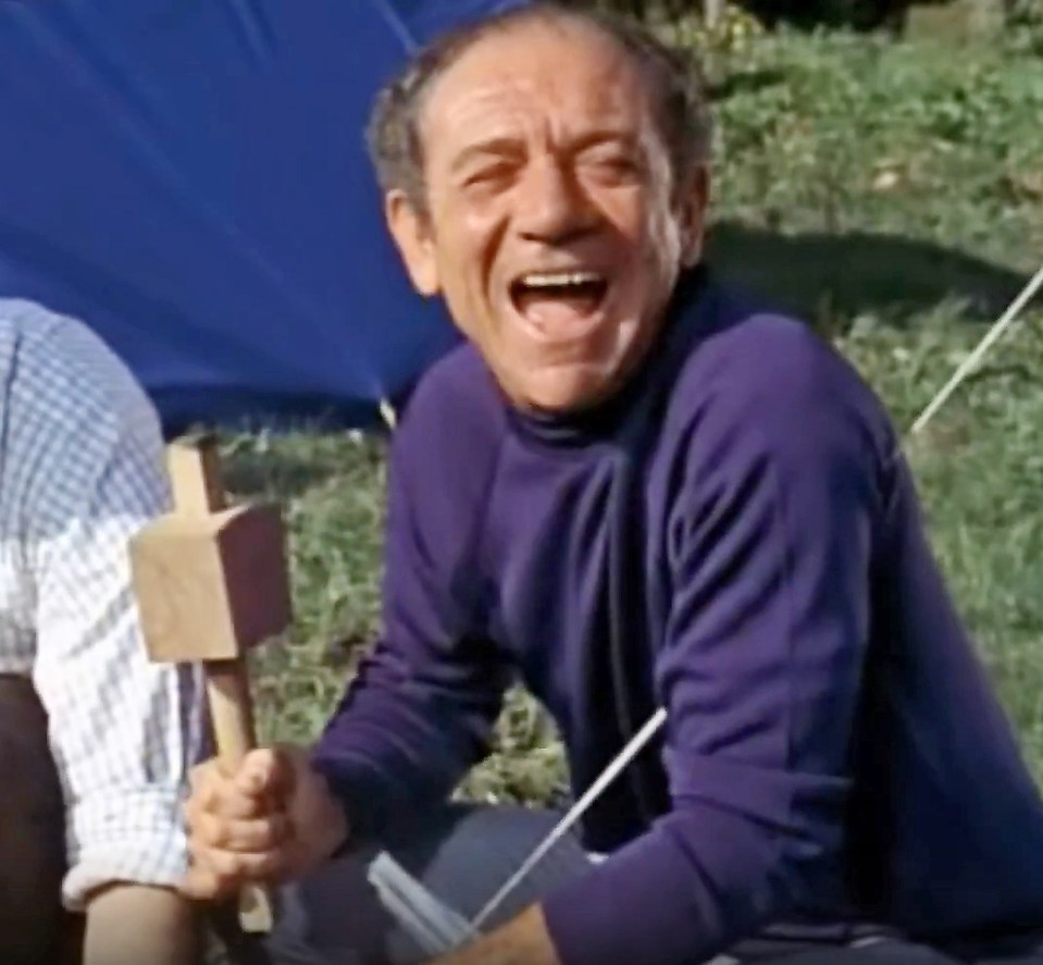 Sid James laughing while holding a mallet in Carry On Camping.