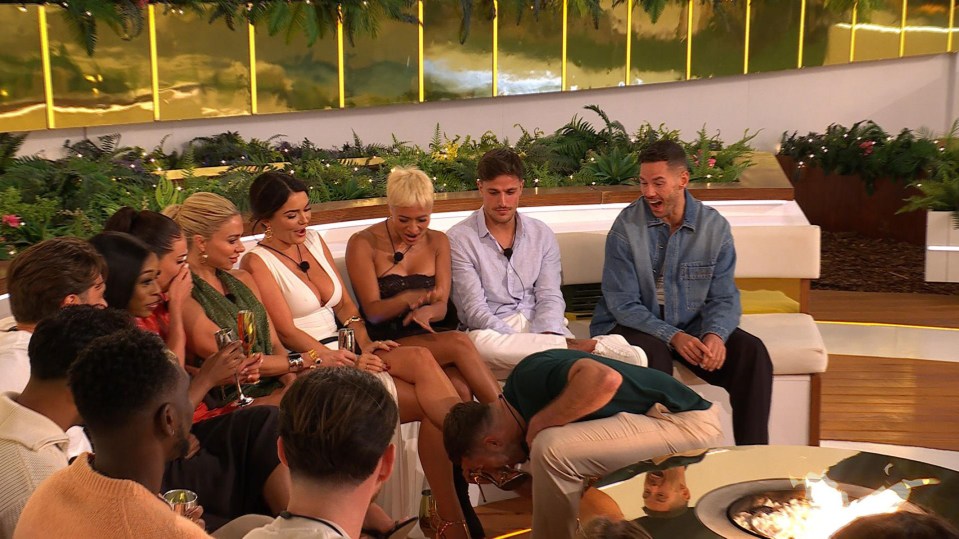 A group of Love Island contestants watching a man kiss a woman's shoe.