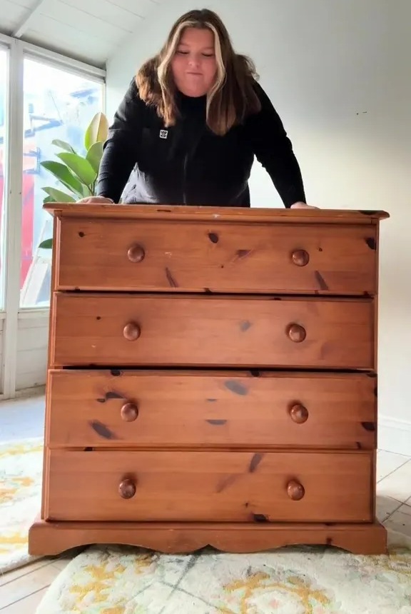 Woman standing behind a wooden dresser.