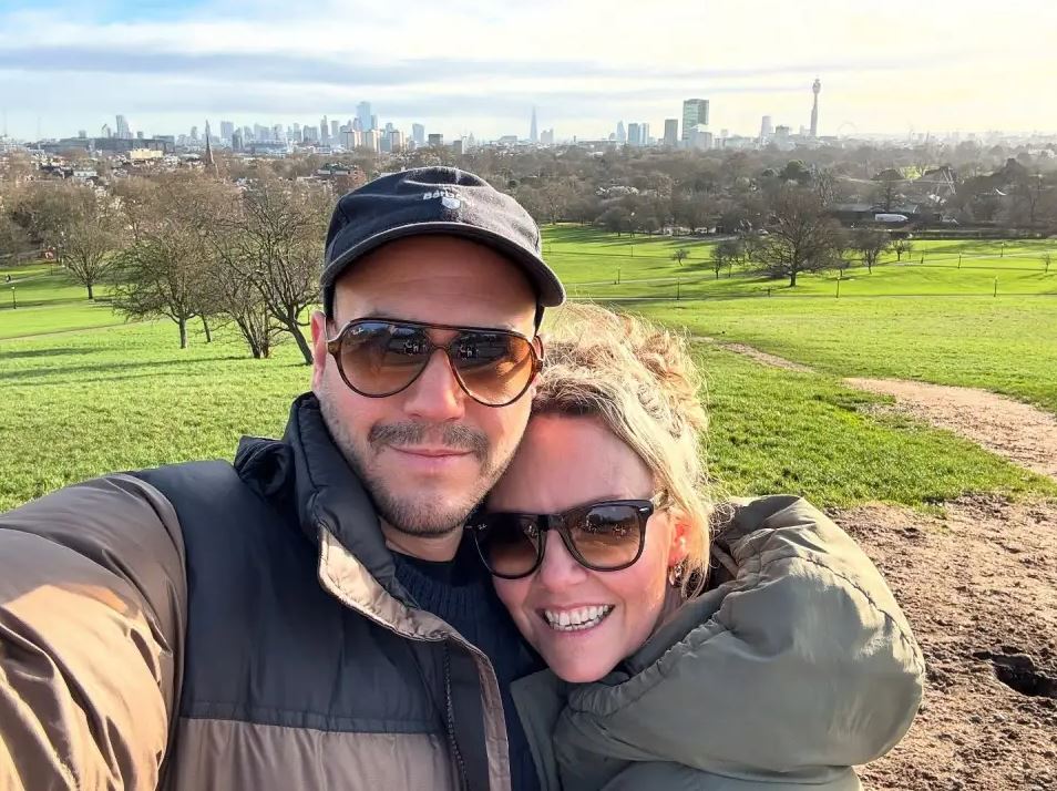 Selfie of a couple in a park with a city skyline in the background.