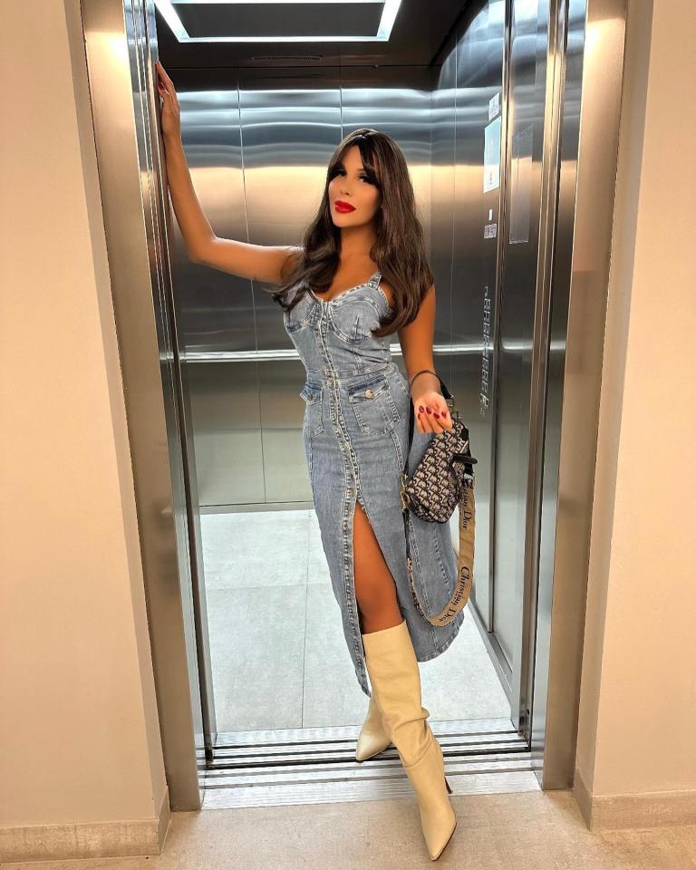 Charlotte Caniggia in a denim dress and cream boots in an elevator.