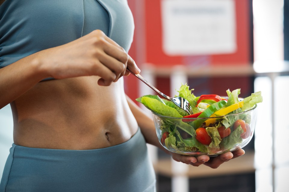 Woman with defined abs holding a bowl of salad.