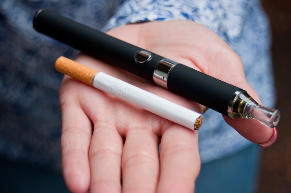 Close-up of a hand holding an e-cigarette and a cigarette.