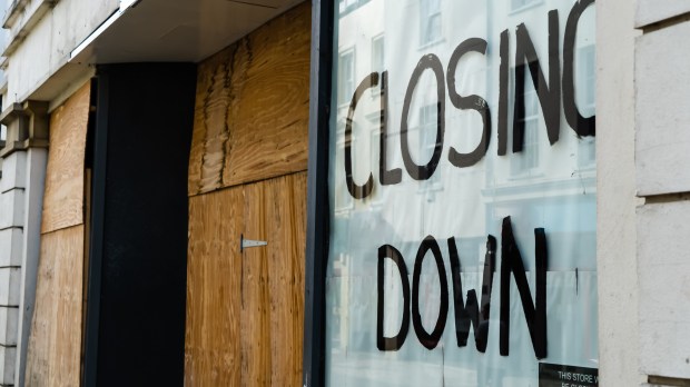 Boarded-up shop window with &quot;Closing Down&quot; painted on it.