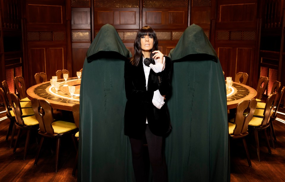 Claudia Winkleman on the set of The Traitors, flanked by two figures in dark robes.