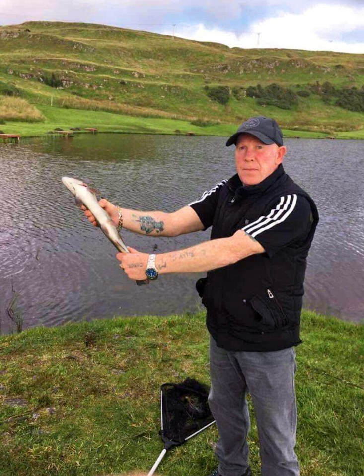 Man holding a fish by a lake.