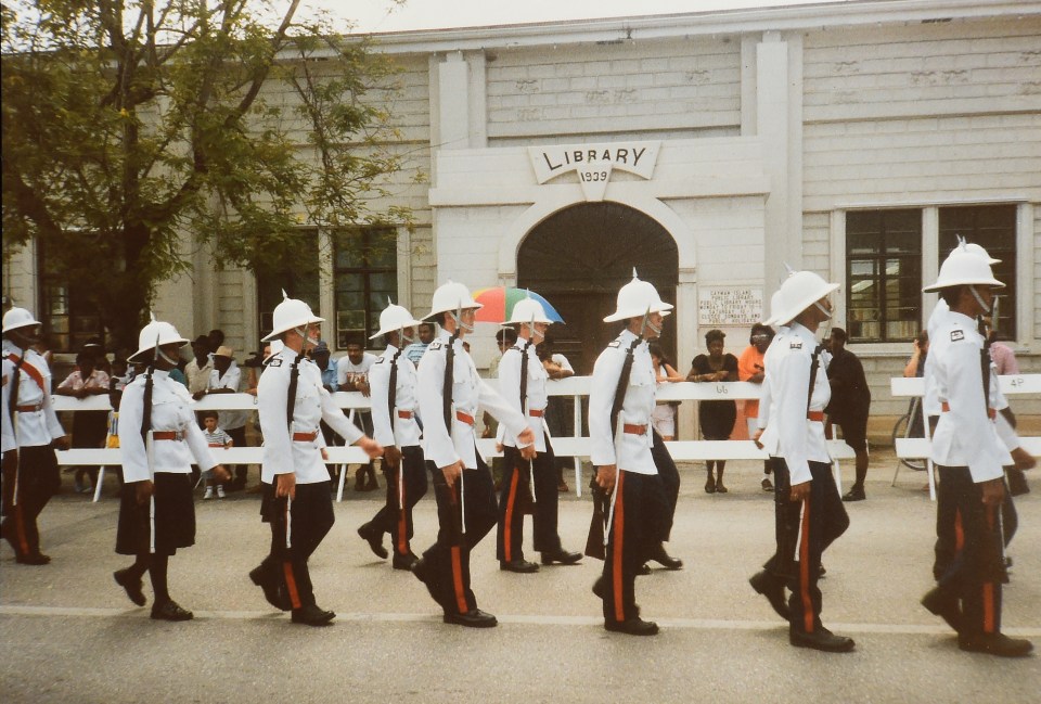 Group photo of uniformed men in front of a building, with palm trees in the background.