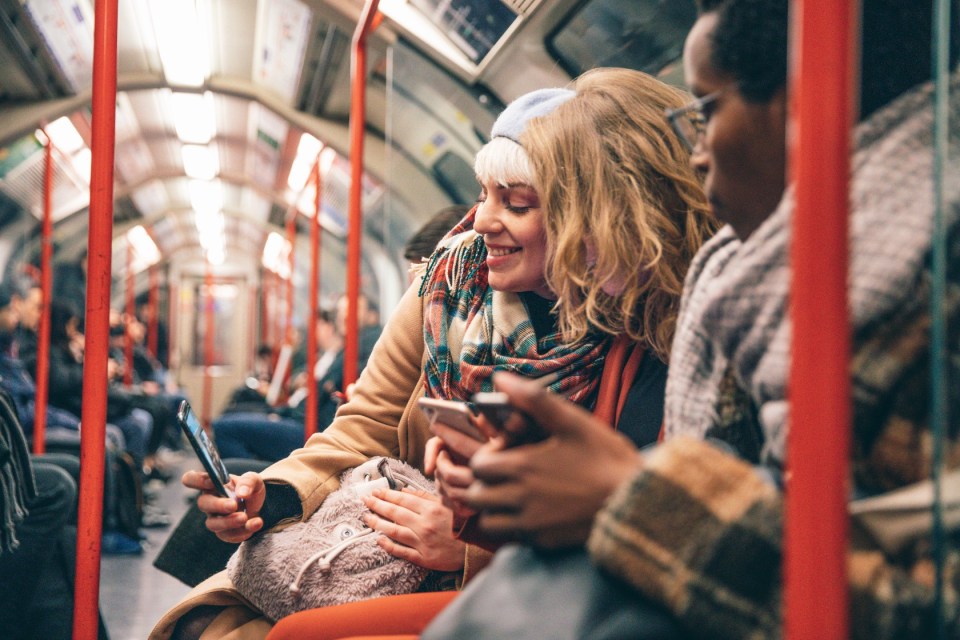 Friends using phones on a London subway.