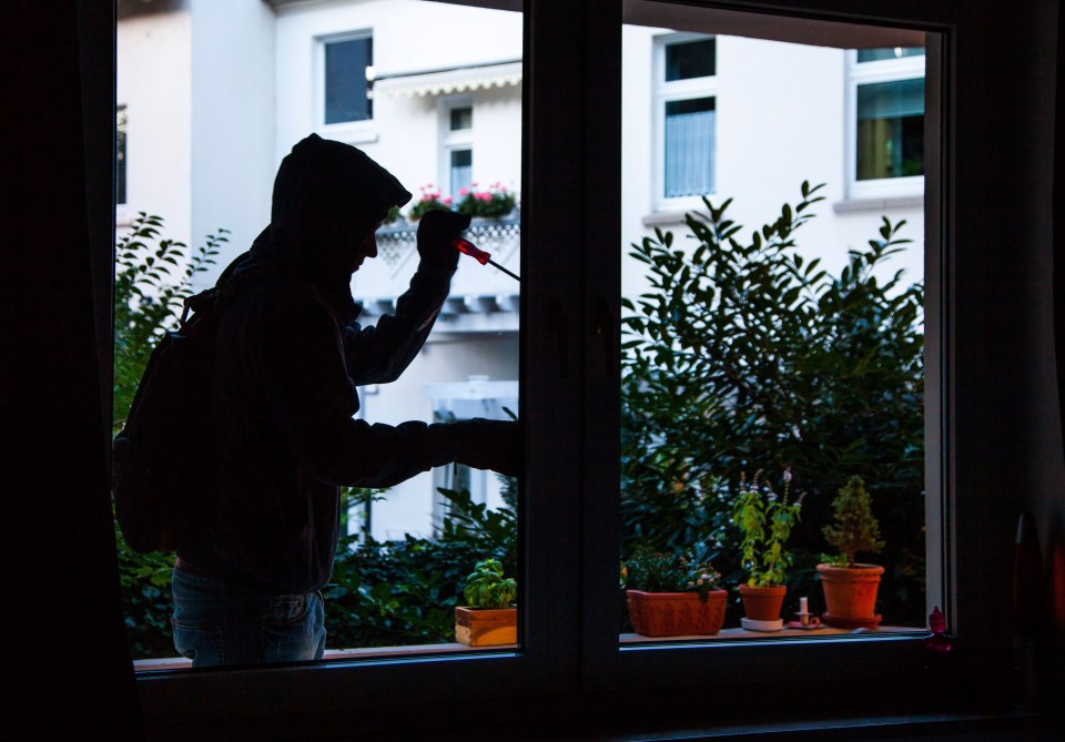 Silhouette of a burglar using a screwdriver to break into an apartment through a window.