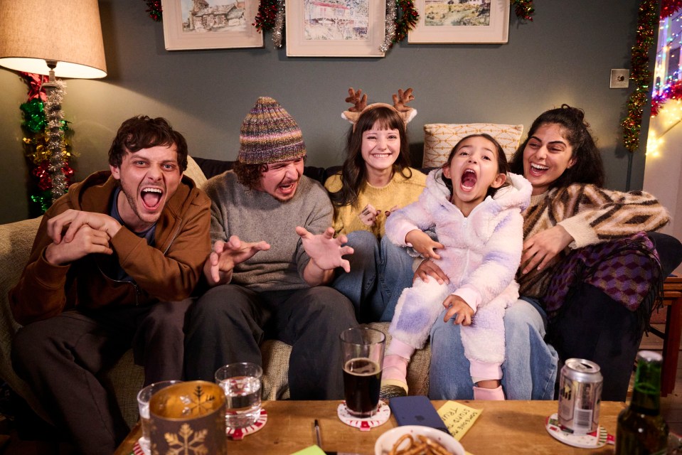 A group of people watch a Christmas special on a couch.