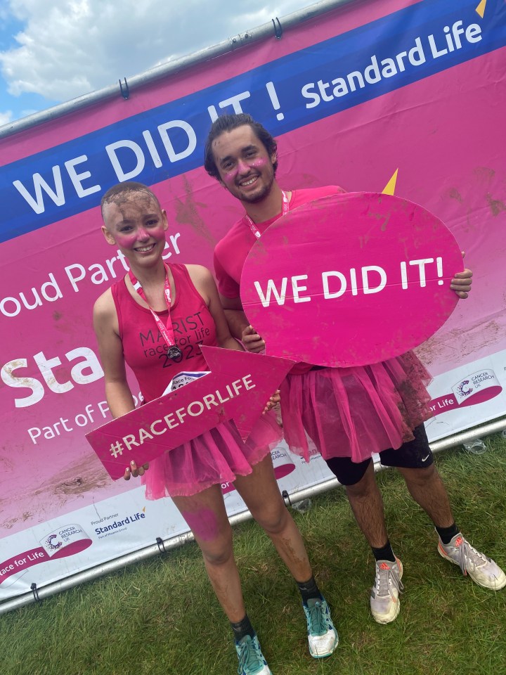 Two muddy participants at a Race for Life event, holding signs that say "We Did It!"