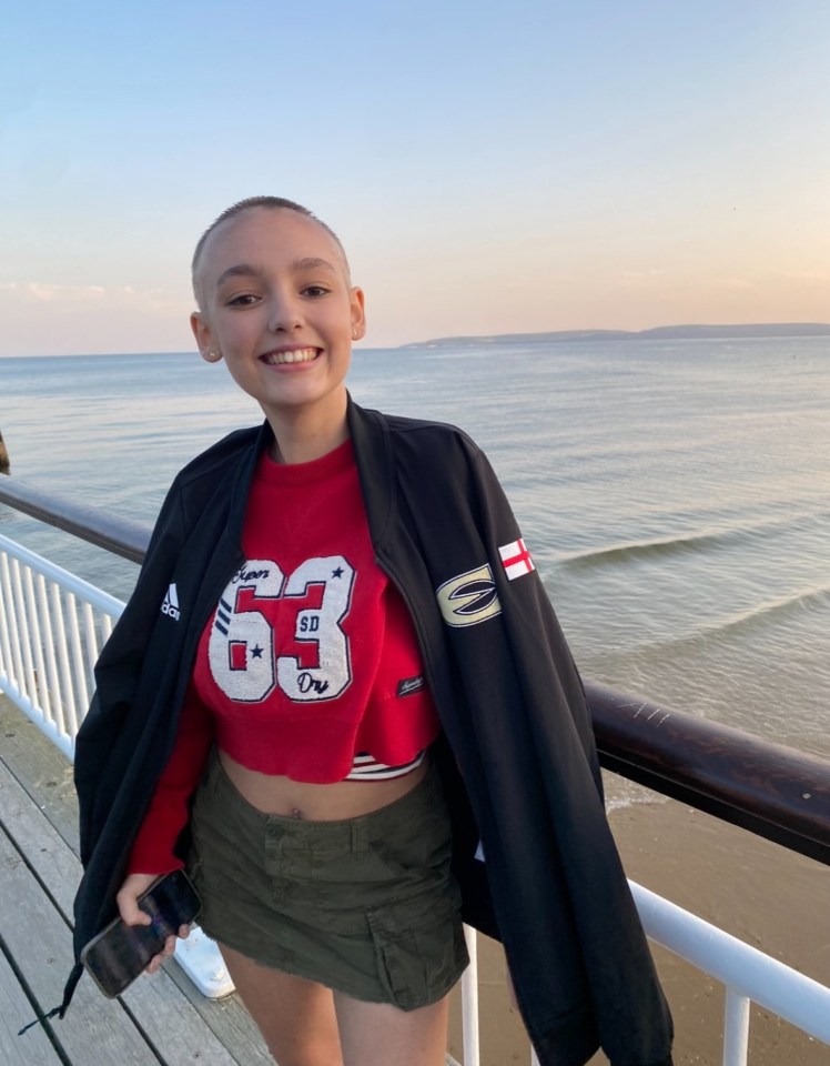 Teenage girl with shaved head smiling on a pier by the ocean.