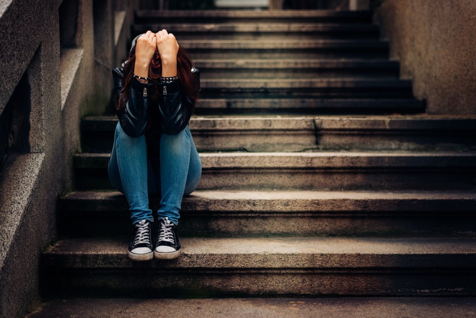 A depressed teenager sits alone on some steps, head in hands.