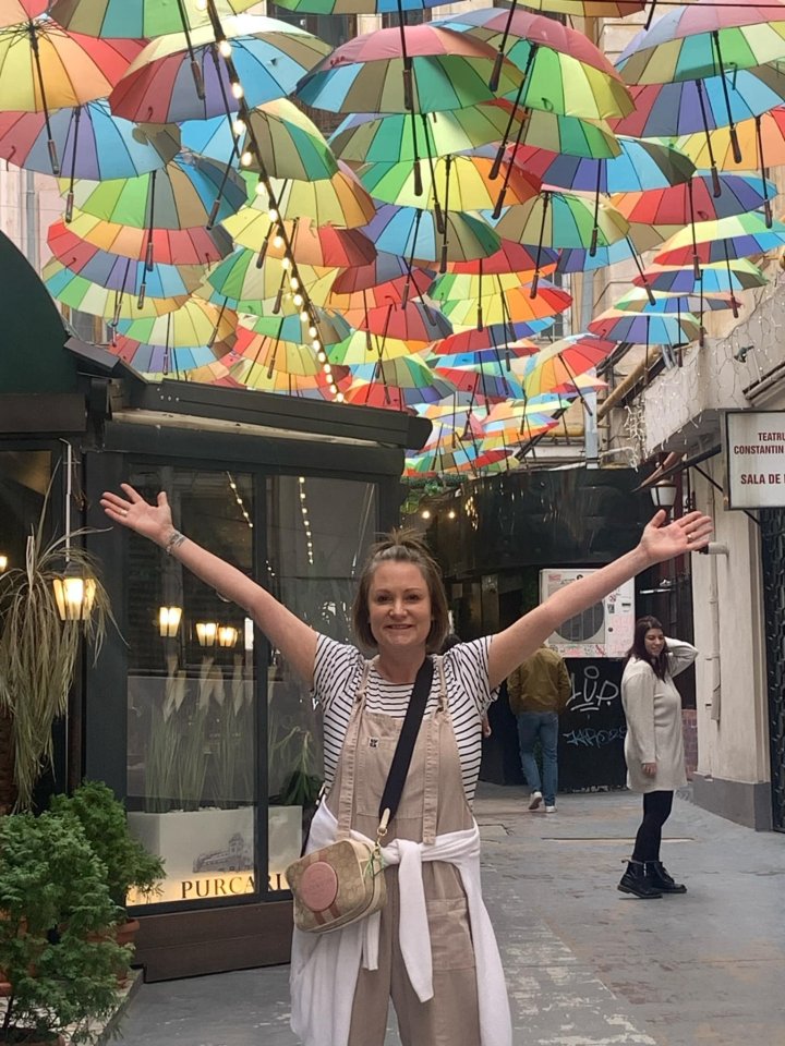 Woman with arms outstretched standing under colorful umbrellas in Bucharest.