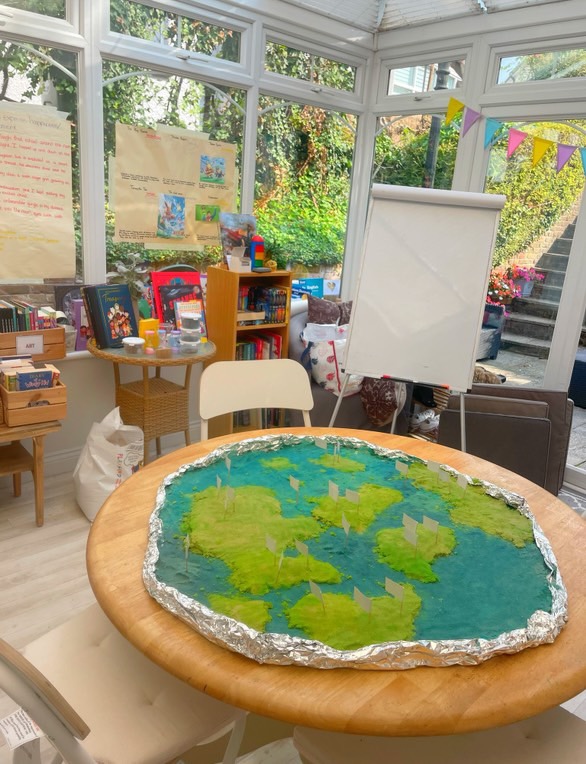 A model world map on a table in a conservatory, surrounded by children's books and learning materials.