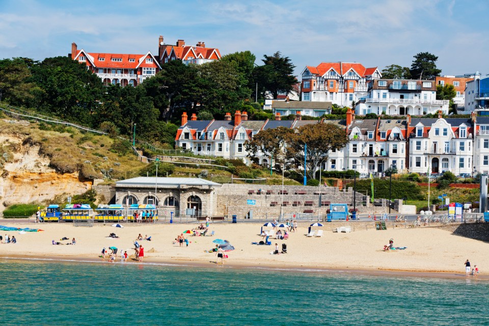 Beach scene in Dorset, England, with houses on a cliff overlooking the sand and ocean.