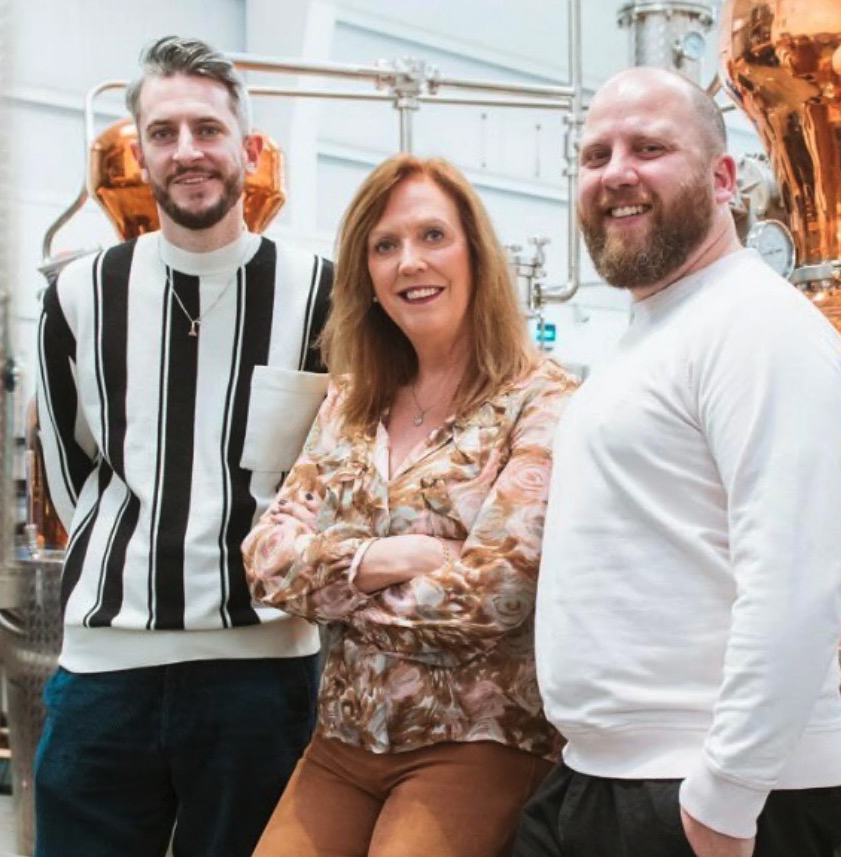 Three people stand in a distillery.