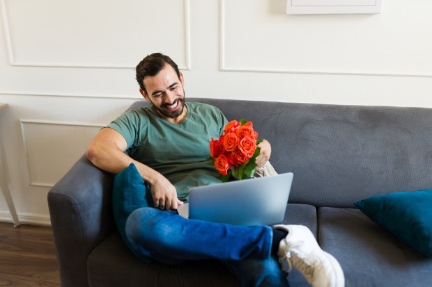 A man on a video call, holding a bouquet of orange roses.