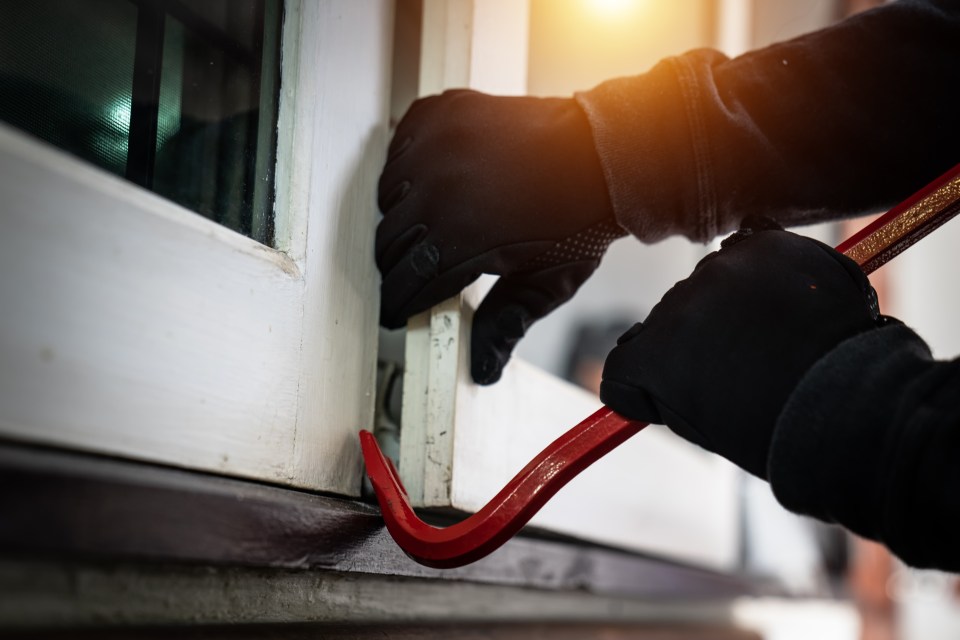 A burglar using a crowbar to break into a house.