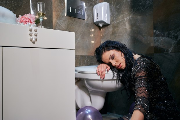 A young woman asleep on a toilet after vomiting.