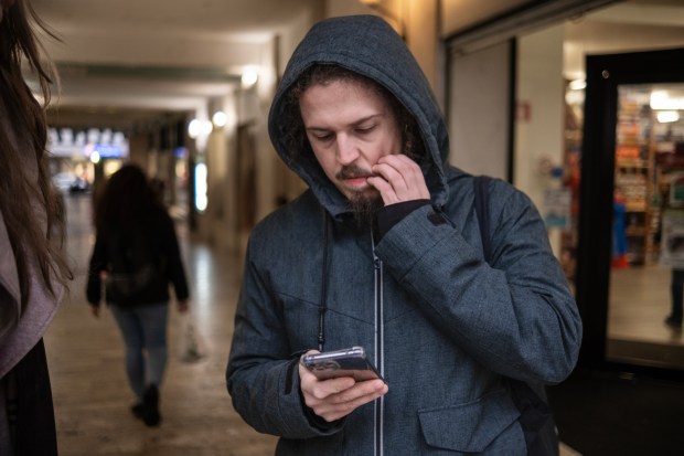 Man in a hooded jacket using his phone in the rain.