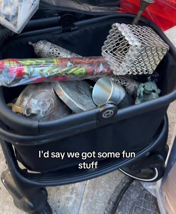 A stroller containing various found items, including metal containers and decorative objects.