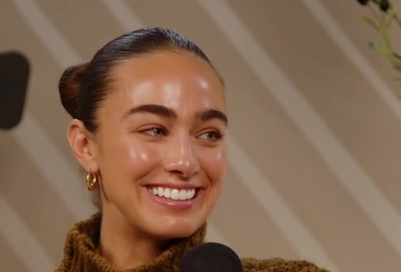 Woman in brown sweater speaks into microphone.