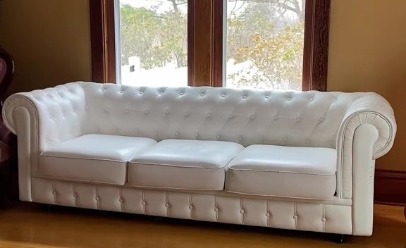 Restored white tufted sofa in a room with hardwood floors and a patterned rug.