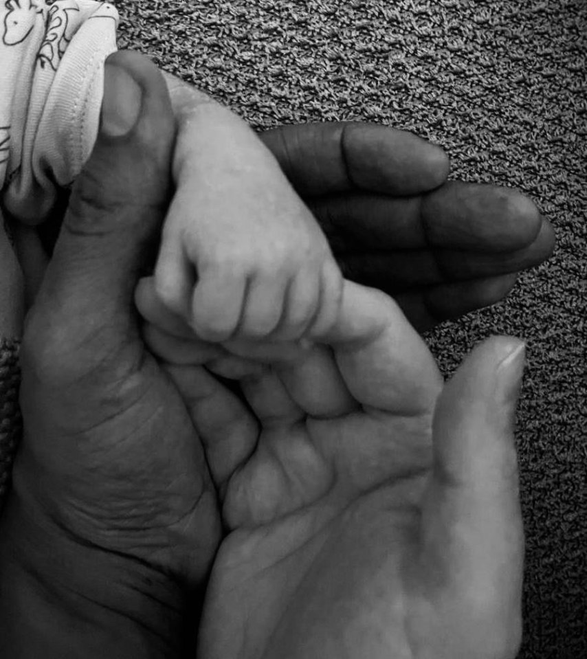 Black and white photo of a newborn's hand grasping an adult's hand.