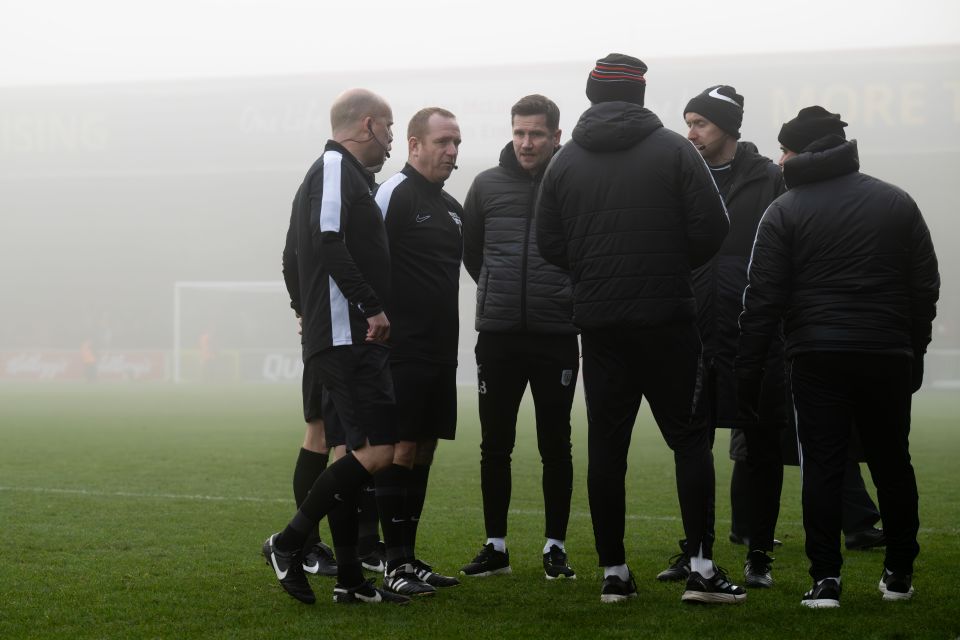 Soccer coaches and referees talking on a foggy field.