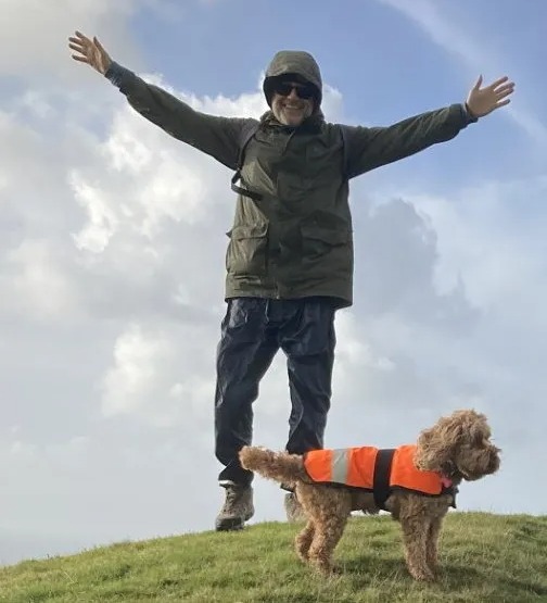 Man with arms outstretched standing on a hill with his dog.