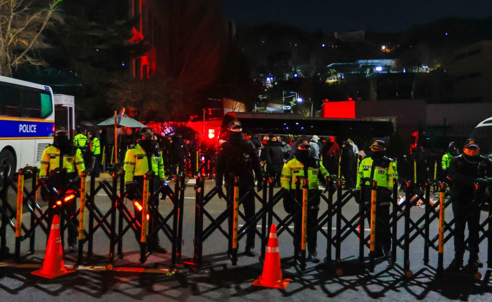 Police officers in South Korea stand behind barricades at night.