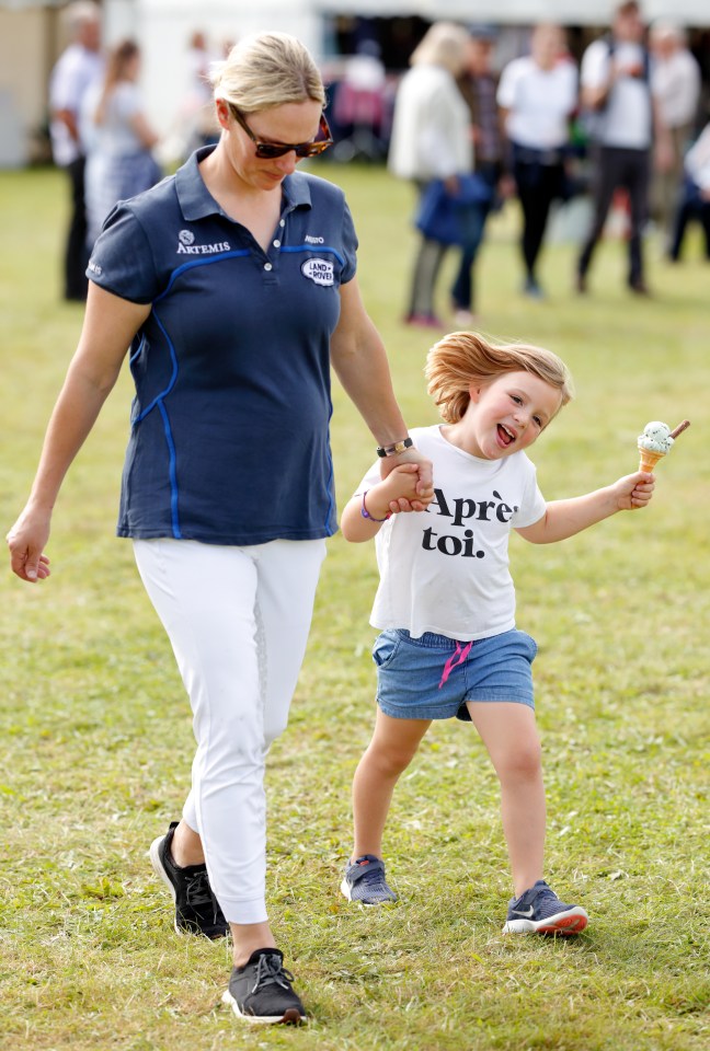 Woman and young girl holding hands walking on grass; girl is eating ice cream.