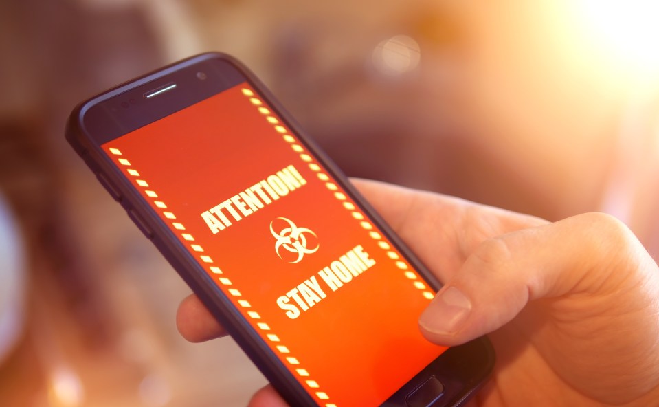 Smartphone displaying an emergency message: "Attention! Stay Home," with a biohazard symbol.