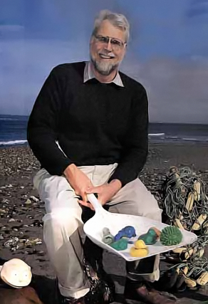 Man holding a scoop with bath toys on a beach.