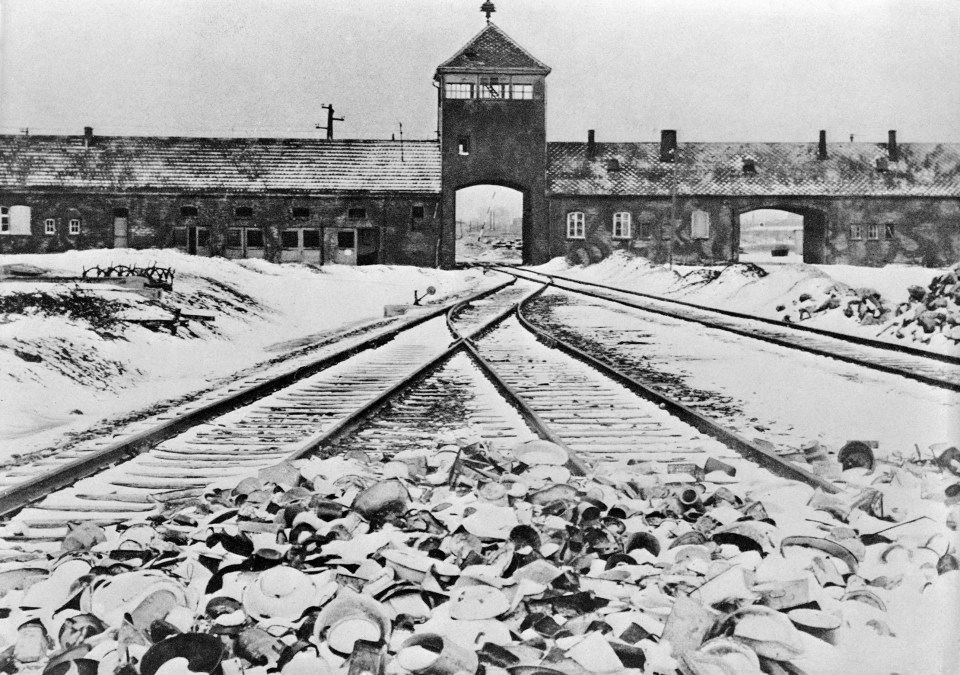 Entrance to Auschwitz-Birkenau concentration camp with train tracks and discarded items in the foreground.