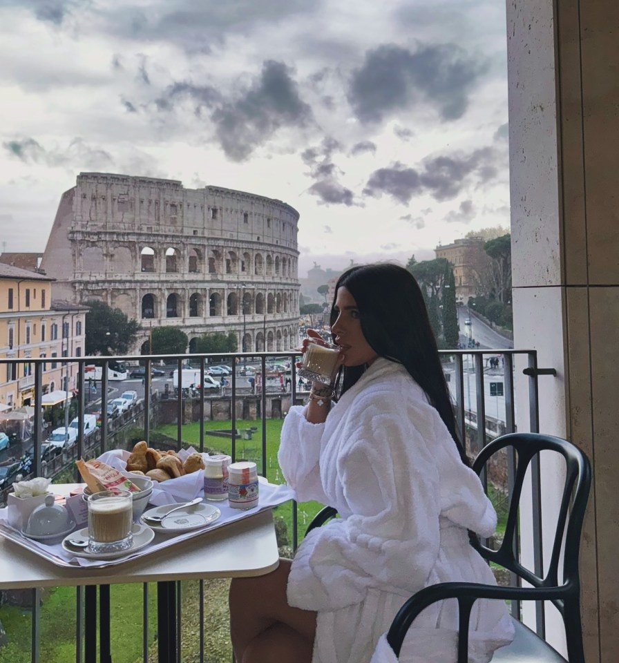 Woman in bathrobe having breakfast on a balcony overlooking the Colosseum.