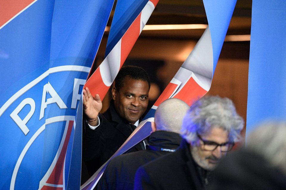 Patrick Kluivert, director of soccer for PSG, waves from behind a Paris Saint-Germain banner.