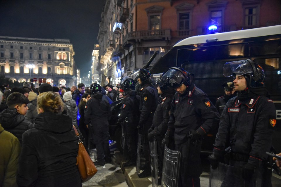 Italian police officers in riot gear stand guard near a cathedral.