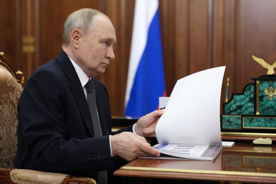 Vladimir Putin reviewing documents at a meeting.