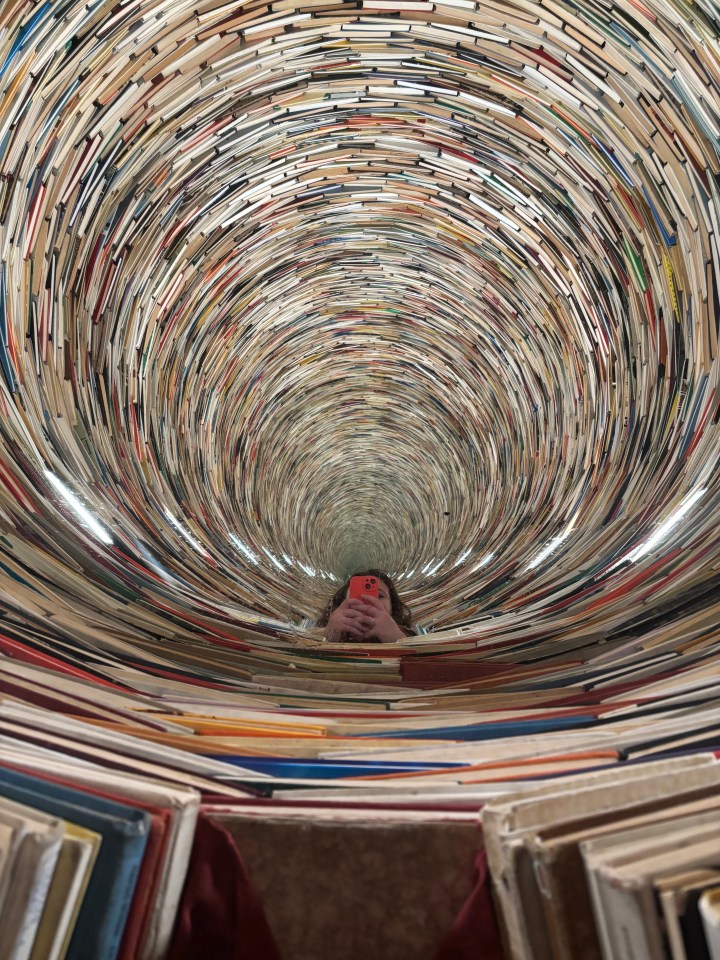 Person taking a selfie in a tunnel of books.