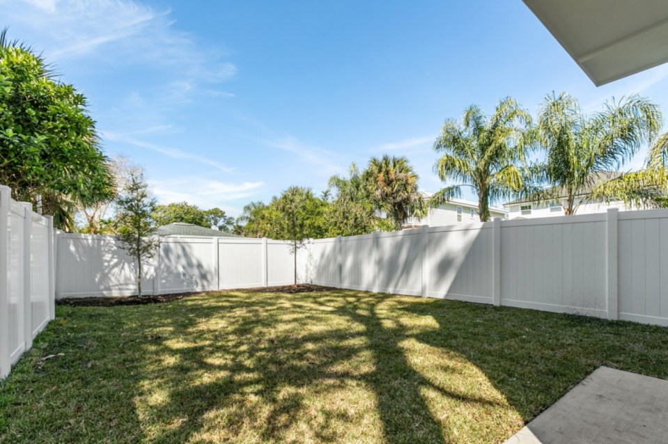 Backyard of a narrow house with a white vinyl fence.