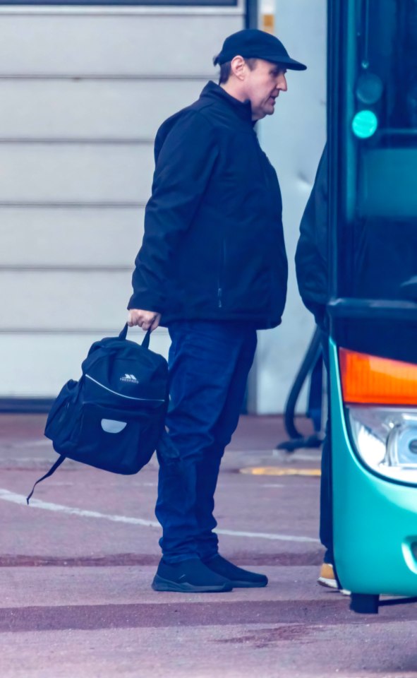 Peter Kay carrying a backpack near a tour bus.