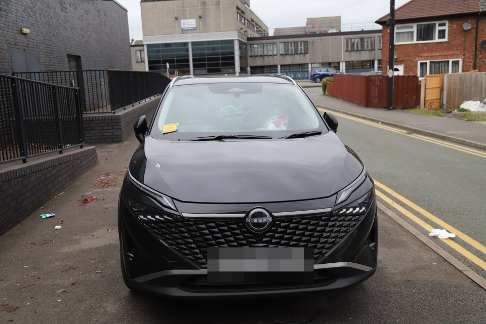 Black Nissan with parking ticket on windshield.