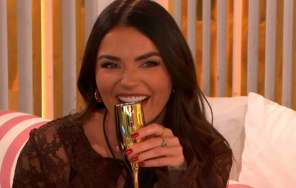 India Reynolds of Love Island All Stars smiling while drinking champagne.