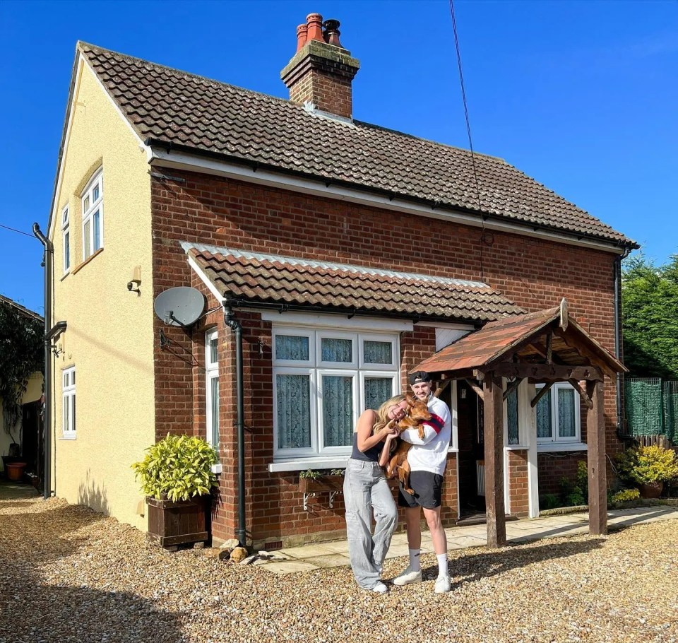 Couple standing in front of their new house with their dog.