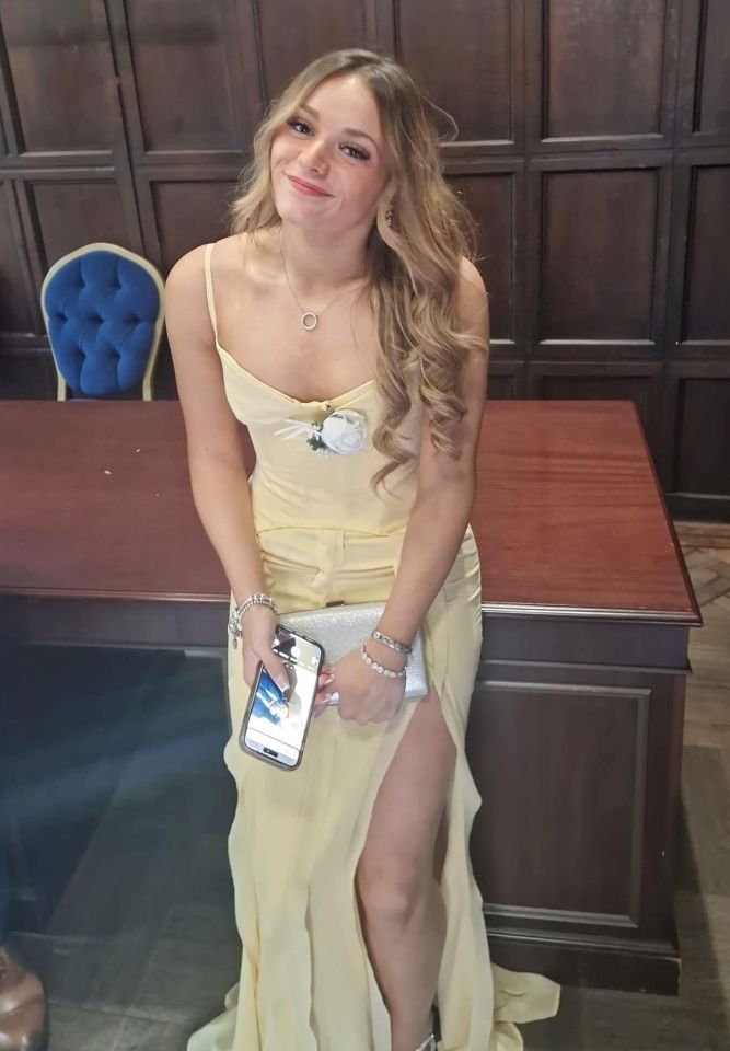 A young woman in a pale yellow dress holds a smartphone and clutch.