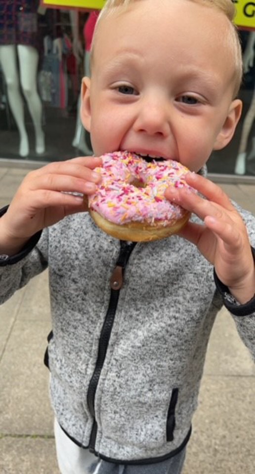 Toddler eating a pink donut with sprinkles.