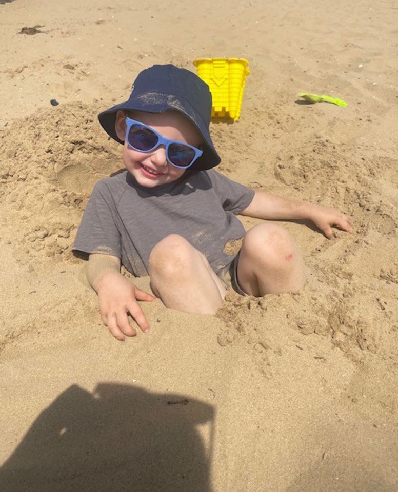 Toddler in sunglasses buried in sand.